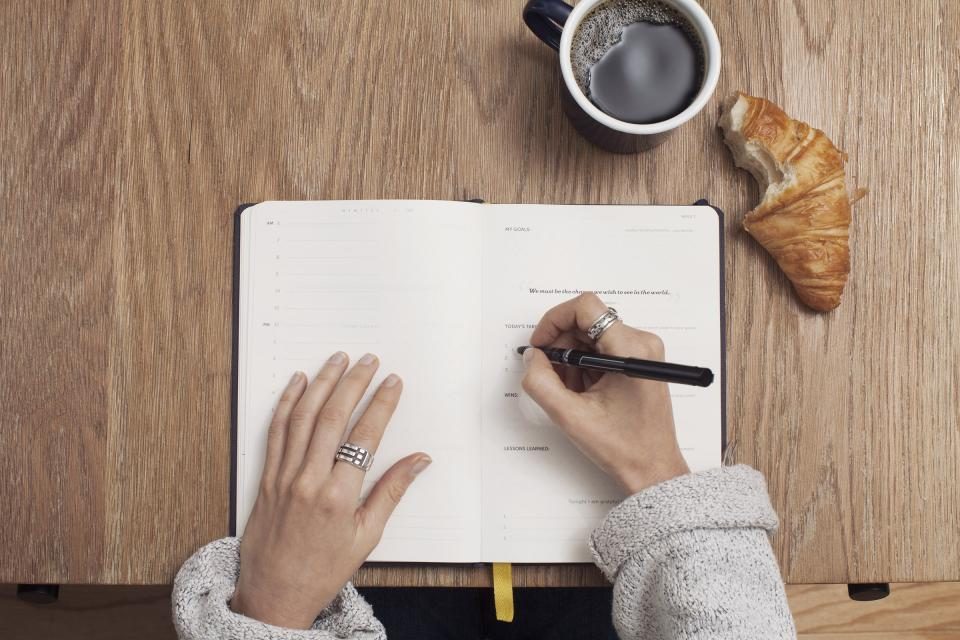 Hænder der skriver i en notesbog ved en kop kaffe